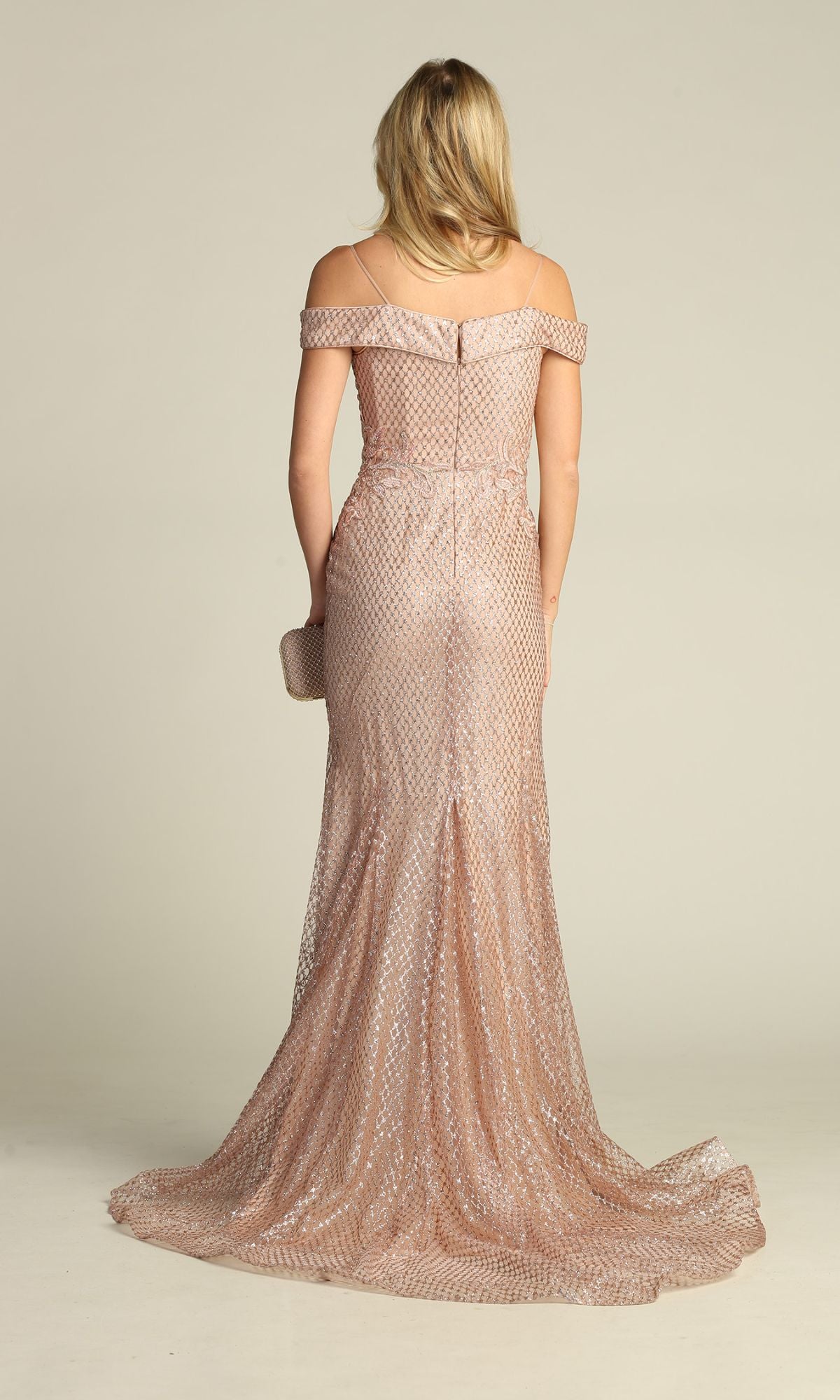 A person stands facing away, holding a small clutch and wearing the Off-the-Shoulder Long Prom Dress: Chicas DM4024—a floor-length, blush pink mermaid gown with a subtle pattern.